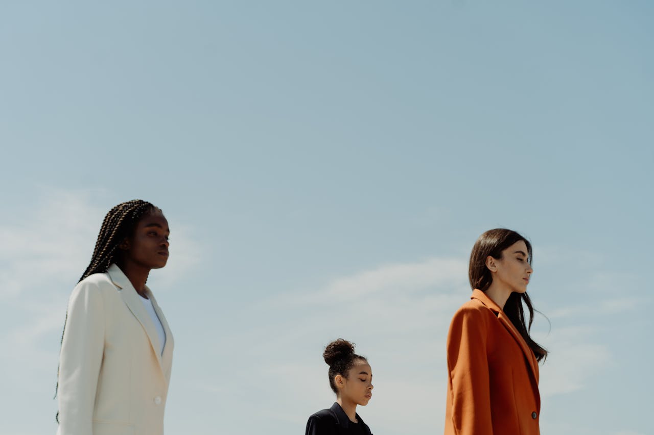 Three fashionable women in stylish blazers standing confidently under a clear sky.