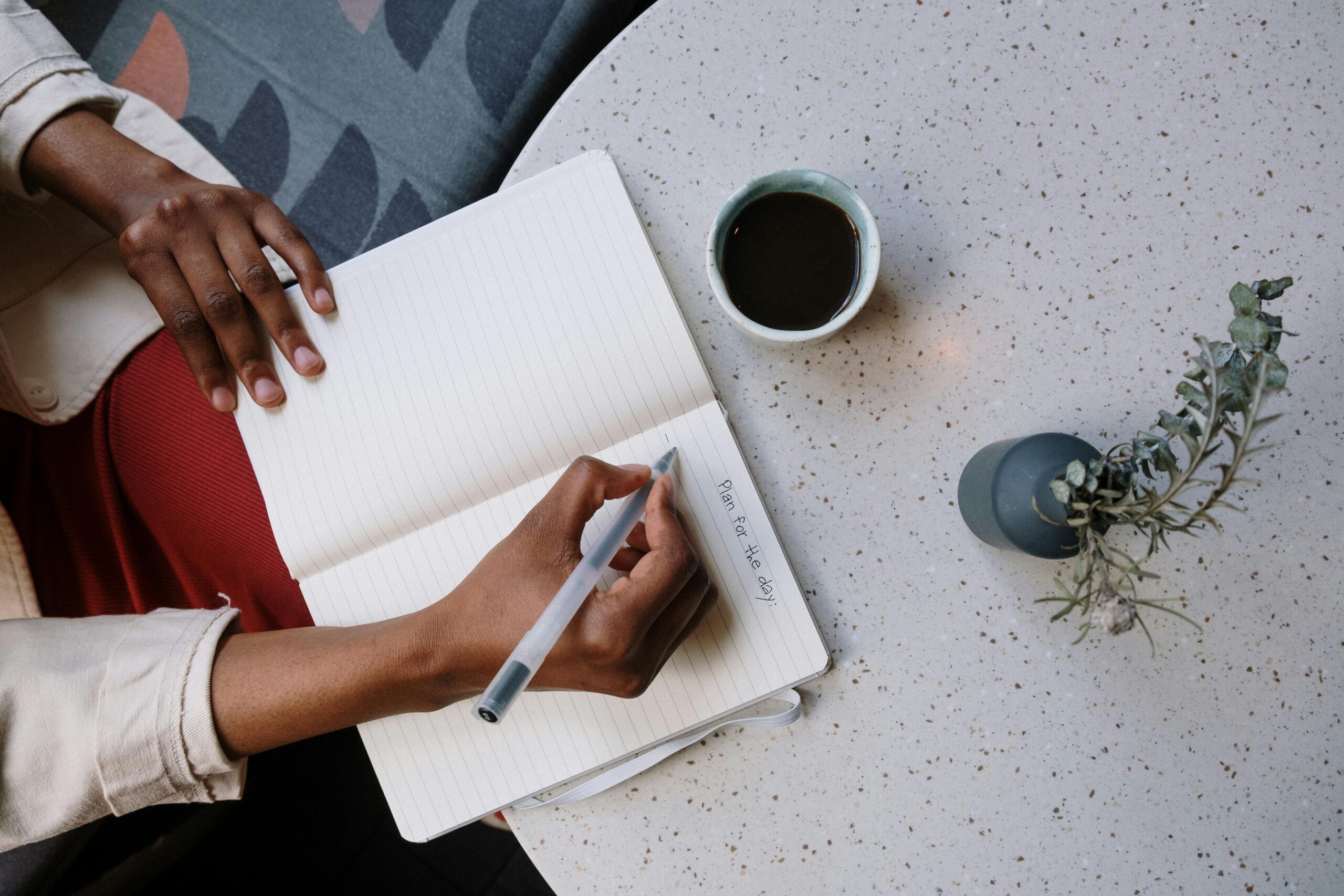 Person writing in a planner with coffee at a café, focusing on planning and productivity.